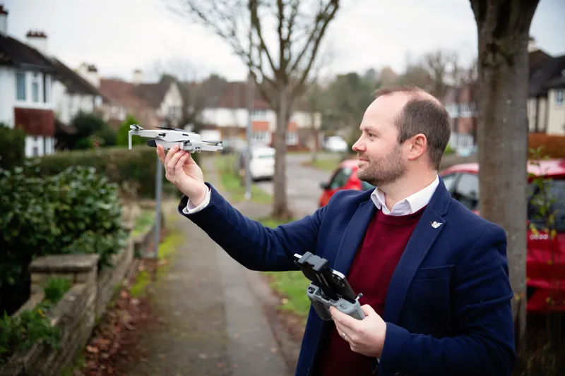A Novello surveyor flying a drone with a handheld controller to inspect a roof from the ground